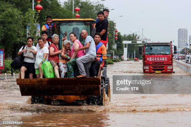 This photo taken on July 26, 2021 shows rescuers evacuating residents with a loader at a flooded area in Weihui, Xinxiang city, in China's central...