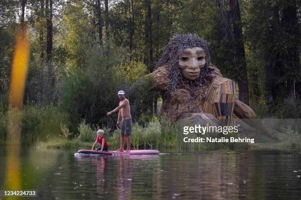 Father and son paddle past "Mama Mimi," a wooden sculpture created by Danish artist Thomas Dambo in Rendezvous Park on July 26, 2021 in Jackson Hole,...
