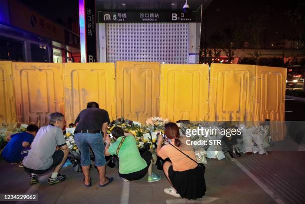 This photo taken on July 26, 2021 shows people placing flowers in front of a subway station as they mourn victims killed in flooding caused by heavy...
