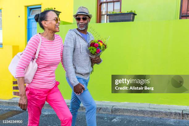 senior couple walking past colourful houses in cape town - man wearing cap photos et images de collection