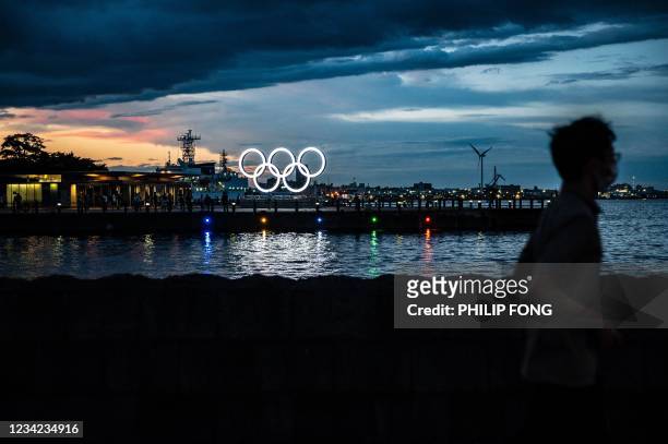 Man walks past the Olympic Rings lit up at dusk in Yokohama on July 27, 2021.