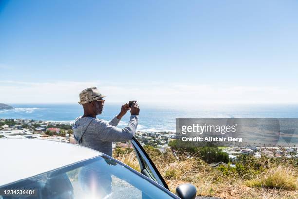 mixed race tourist photographing sea view with smart phone - auto mieten stock-fotos und bilder