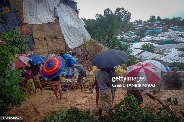 Onlookers stand as Rohingya refugees work amid the debris of houses in Balukhali camp on July 27, 2021 that were damaged after monsoon rains...