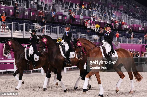 Gold medallists Dorothee Schneider of Germany, Isabell Werth of Germany and Jessica von Bredow-Werndl of Germany wave as they ride together with...