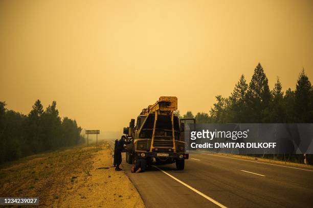 Men repair their truck in smoke from a forest fire on a road near Magaras, in the republic of Sakha, Siberia, on July 27, 2021. - Russia is plagued...