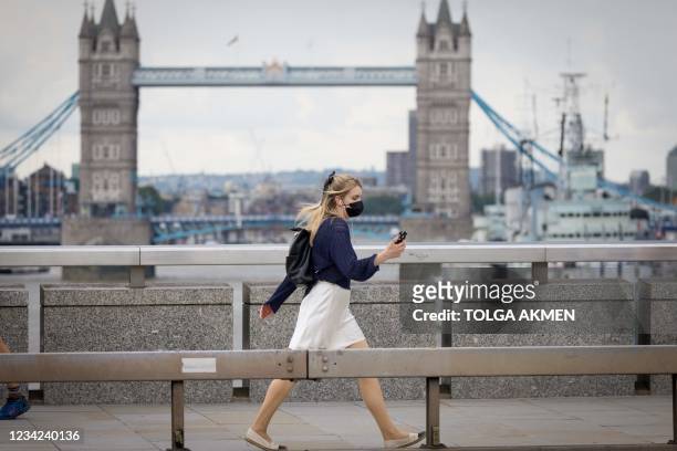 Pedestrian wearing a face mask walks across London Bridge in central London on July 27, 2021. - Prime Minister Boris Johnson called for caution...