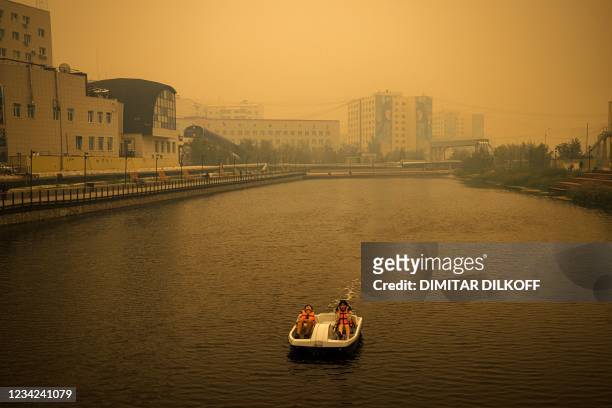 Couple rides a pedal boat as smoke from nearby forest fires hangs over the city of Yakutsk, in the republic of Sakha, Siberia, on July 27, 2021. -...