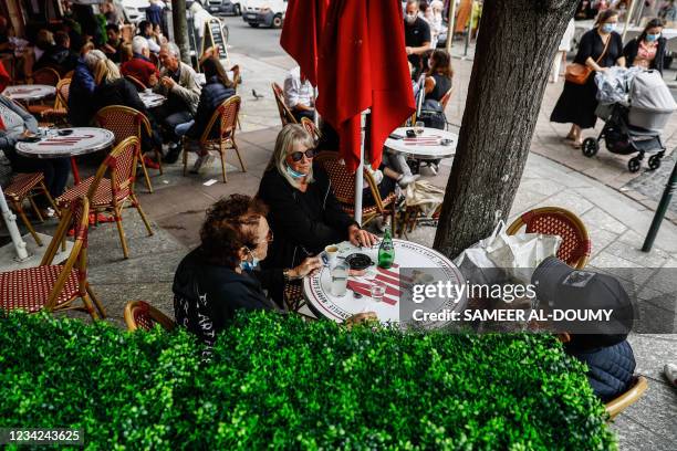 People sit around a table at a coffee shop after showing their Covid-19 health pass in Deauville on July 27, 2021. - France's highest constitutional...