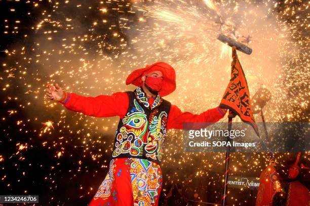 Man disguised as a devil and wearing a facemask is seen under a shower of sparks holding a pyrotechnic stick during the Cercavila del Foc in...
