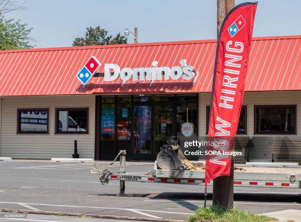 A now hiring sign is seen outside of a Domino's pizza...