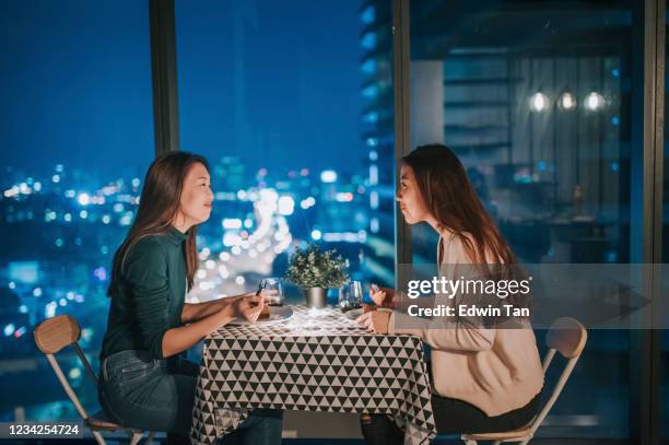 an lgbt couple enjoying their drink with city view at background at night on candlelight date - table for two stock pictures, royalty-free photos & images