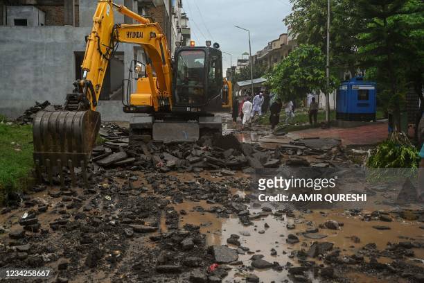 Workers use an earth-mover to clear debris from a road damaged in the flood waters after heavy monsoon rains in Islamabad on July 28, 2021.