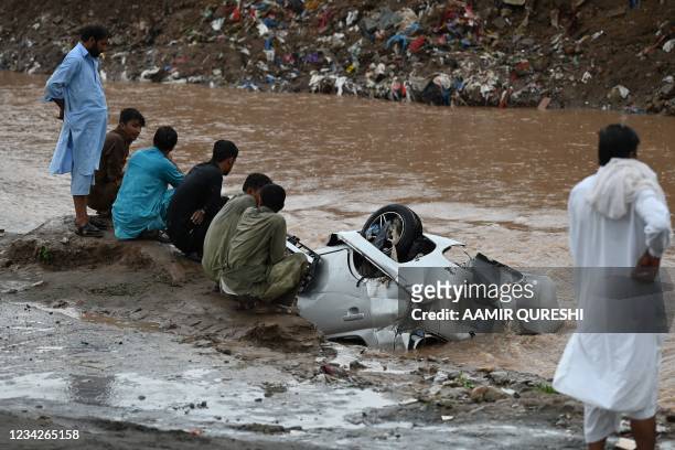 Residents gather as they look at a damaged car submerged in flood waters after heavy monsoon rains in Islamabad on July 28, 2021.