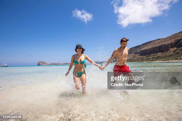 Young couple enjoys the water of Balos, as they run or walk in the water of Balos Beach, the incredible lagoon, with the pool like turquoise exotic...