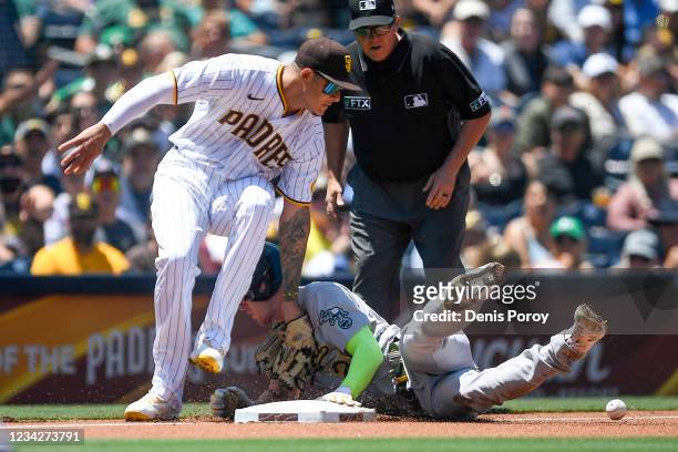 Mark Canha of the Oakland Athletics slides into third base as Manny Machado of the San Diego Padres drops the ball during the first inning of a...