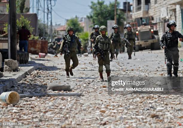 Israeli soldiers and border guards walk along a street littered with stones during clashes with Palestinian protesters in the town of Beit Ummar,...