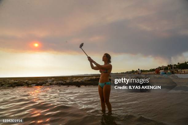 Woman takes a selfie on the beach as smoke billows from a massive forest fire which engulfed a Mediterranean resort region on Turkey's southern coast...