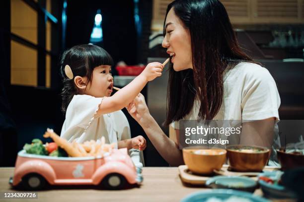 happy little asian girl enjoying her kids meal set with her mother in a restaurant. they are feeding each other with french fries and having a enjoyable time together - mother and child snacking stockfoto's en -beelden