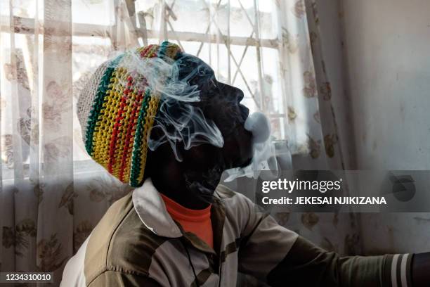 Man blows smoke after inhaling crystal meth from his home made meth pipe at the back of a house commonly referred to as a drug base where drug users...