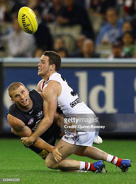 Lachie Henderson of the Blues handballs whilst being tackled by Jack Steven of the Saints during the round 24 AFL match between the Carlton Blues and...