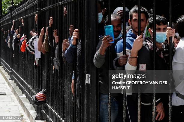 Migrants and homeless people wait behind the fences of the Place des Vosges in Paris, on July 30 to be relocated after spending the night in tents...