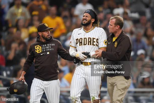 Fernando Tatis Jr. #23 of the San Diego Padres is helped off the field by manager Jayce Tingler and a trainer after he was injured during the first...