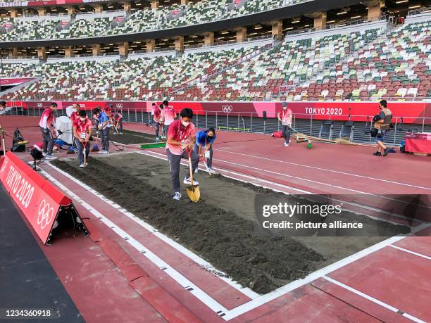 August 2021, Japan, Tokio: Athletics: Olympics, long jump, women, qualification, at the Olympic Stadium. Helpers digging the pit for the long jump....