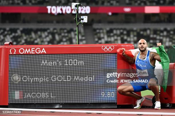 Italy's Lamont Marcell Jacobs poses next to the scoreboard displaying his gold medal result after winning the men's 100m final during the Tokyo 2020...