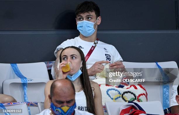 British diver Thomas Daley sits with his knitting as he watches divers in the preliminary round of the men's 3m springboard diving event during the...