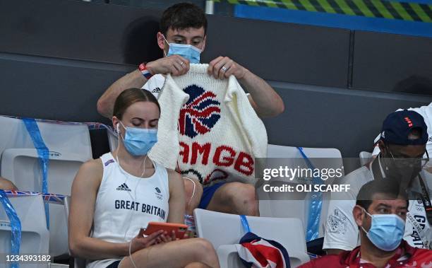 British diver Thomas Daley sits with his knitting as he watches divers in the preliminary round of the men's 3m springboard diving event during the...