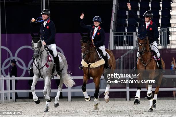 Britain's team Tom McEwen, Laura Collett and Oliver Townend display their gold medals as they ride in the ring after winning the the equestrian...
