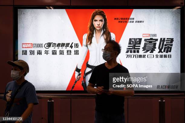 Commuters stand in front of a commercial banner from Disney's and Marvel Studios movie of Black Widow, played by Scarlett Johansson, at MTR subway...