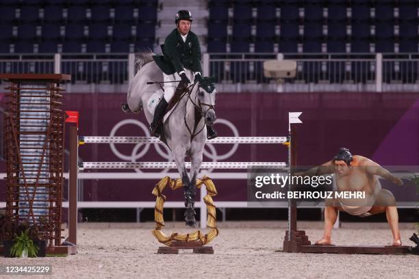 Ireland's Cian O'Connor rides Kilkenny past a small sumo wrestler statue in the equestrian's jumping individual qualifying during the Tokyo 2020...