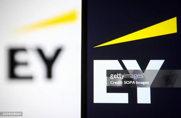 In this photo illustration an EY logo is seen on a smartphone and a pc screen.
