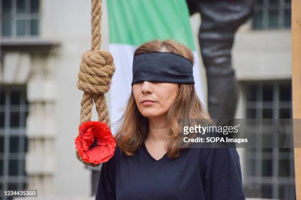 Blindfolded demonstrator stands next to a noose with a red poppy flower during the Iran protest. Members of the Anglo-Iranian community and...