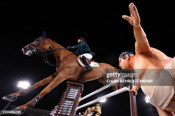 Brazil's Marlon Modolo Zanotelli riding Edgar M competes past a small sumo wrestler statue in the equestrian's jumping individual qualifying during...