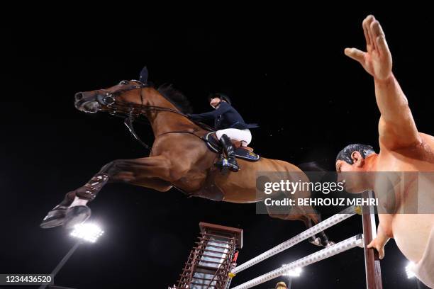 Sweden's Peder Fredricson riding All In competes past a small sumo wrestler statue in the equestrian's jumping individual qualifying during the Tokyo...