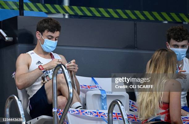 Britain's Thomas Daley knits as he sits and watches the preliminary round of the women's 10m platform diving event during the Tokyo 2020 Olympic...
