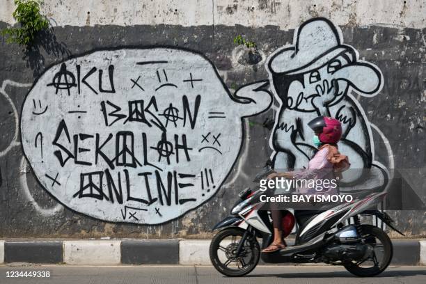 Woman rides her motorbike past a mural reading "I'm bored of home schooling" in Jakarta on August 4 as schools have held online classes for more than...