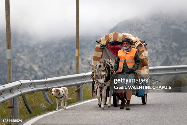 This photograph taken on July 8, 2021 shows a man walking along the road with his dog and his donkey, towing a small caravan in the Pyrenees...