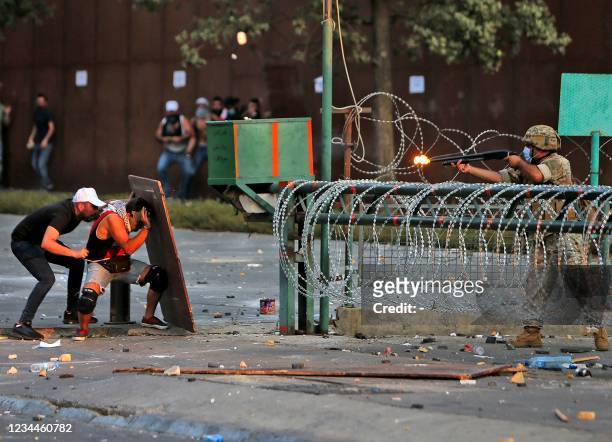 Protesters take cover behind a wooden board as an army soldier fires a load of rubber bullets during clashes near the Lebanese parliament...