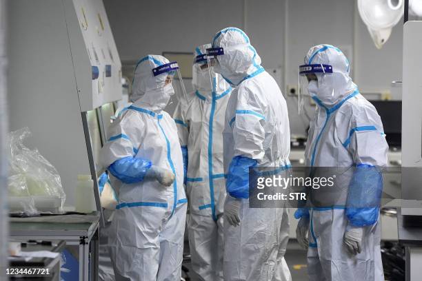 This photo taken on August 4, 2021 shows laboratory technicians wearing personal protective equipment working on samples to be tested for the...