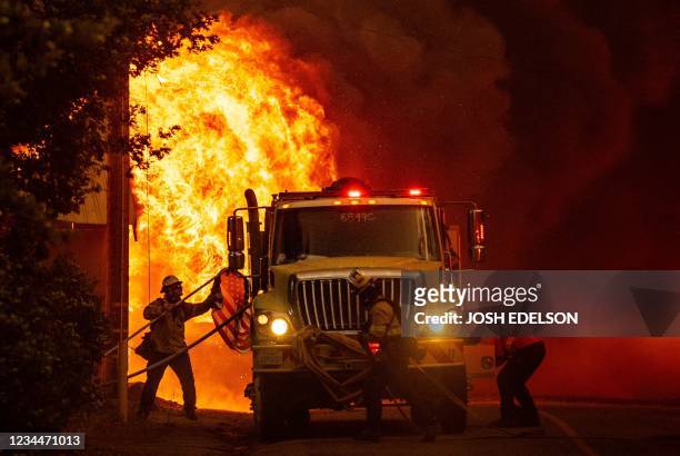 Christopher Moore, a firefighter from San Diego, saves an American flag as flames consume a home during the Dixie fire in Greenville, California on...