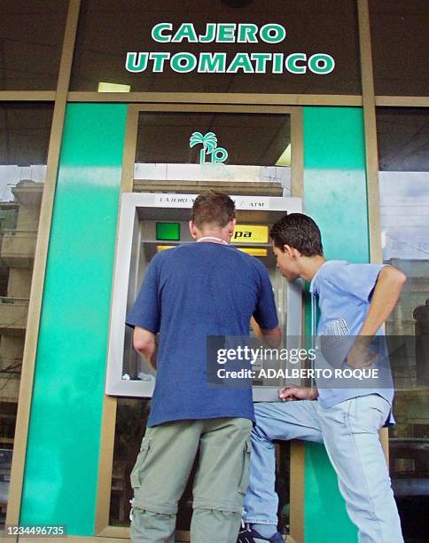 Two young men are seen using a teller machine in La Habana, Cuba 23 October 2001. ACOMPANA NOTA: " ECONOMIA DE CUBA SE DETERIORA TRAS IMPACTO DE...