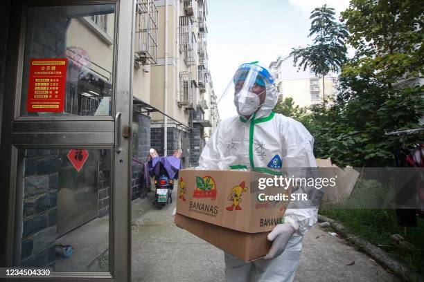 Volunteers and staff members wearing personal protective equipment against the spread of Covid-19 coronavirus carry foods and daily necessities as...