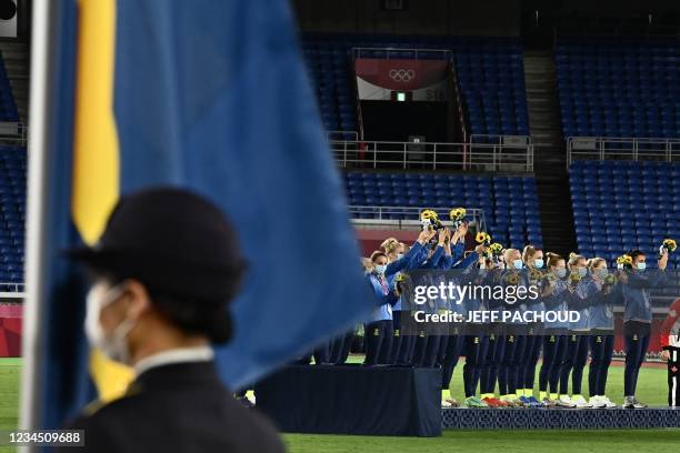 The Sweden national flag is seen in the foreground as silver medallists Sweden's team stand on the podium for the victory ceremony after the Tokyo...