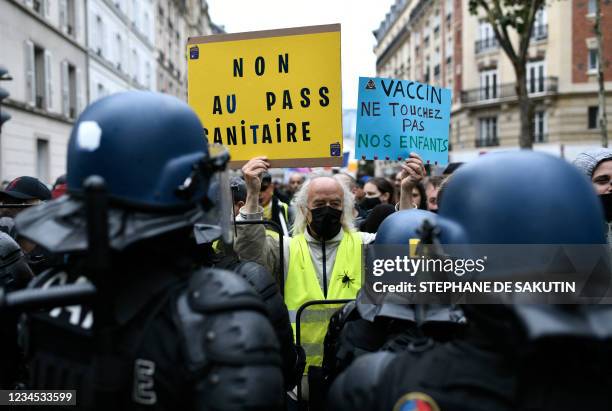 Protestor holds signs reading 'No to the health pass' and 'Vaccine : keep away from our children' in front of riot forces during a demonstration,...
