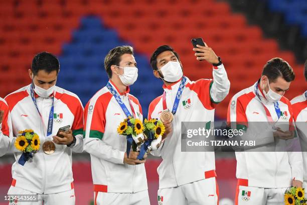 Mexico's bronze medallists use their mobile phones on the podium during the medal ceremony of the Tokyo 2020 Olympic Games men's football competition...