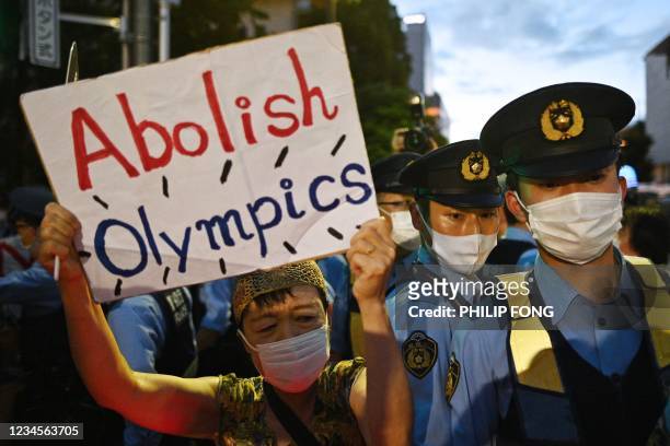 Demonstrator walks past police officers as she holds up a sign against Tokyo 2020 Olympic Games ahead of the closing ceremony outside the Olympic...