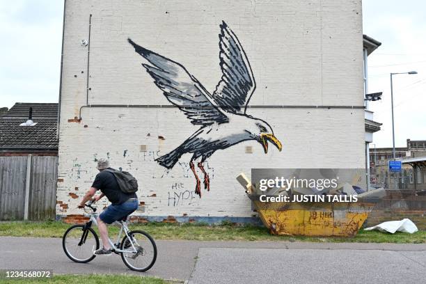 Cyclist rides past a stensil of a gull about to swoop down onto a carton of chips, the subject of a graffiti artwork bearing the hallmarks of street...